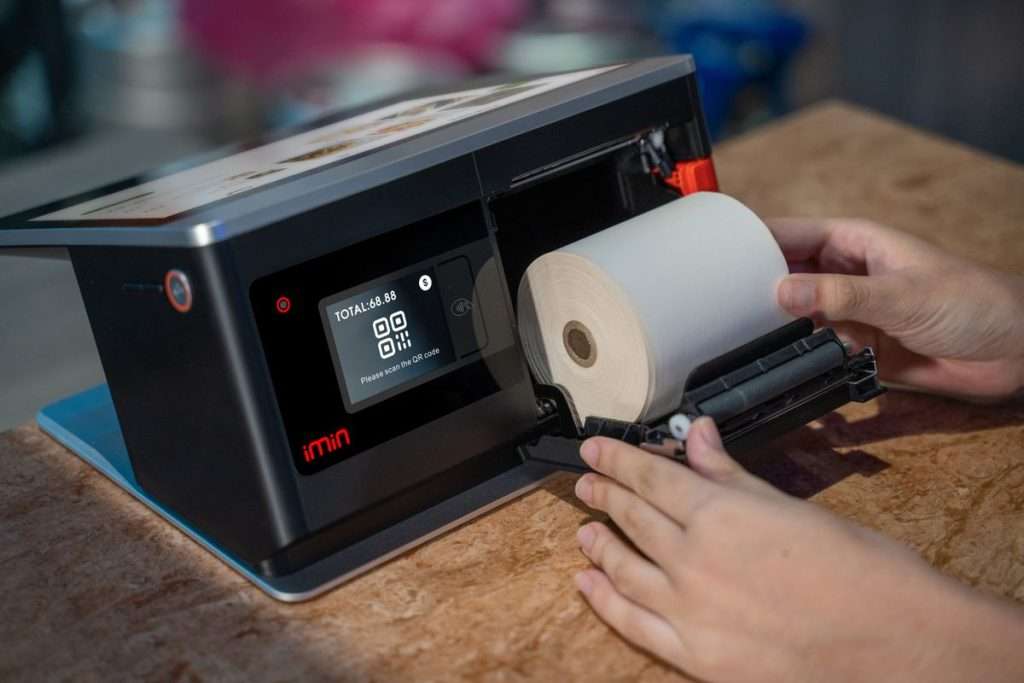 Mãos a colocar um rolo de papel térmico num terminal POS com ecrã tátil