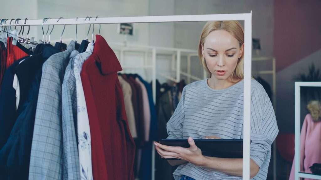 Funcionária de uma loja de roupa a consultar um tablet junto de um cabide