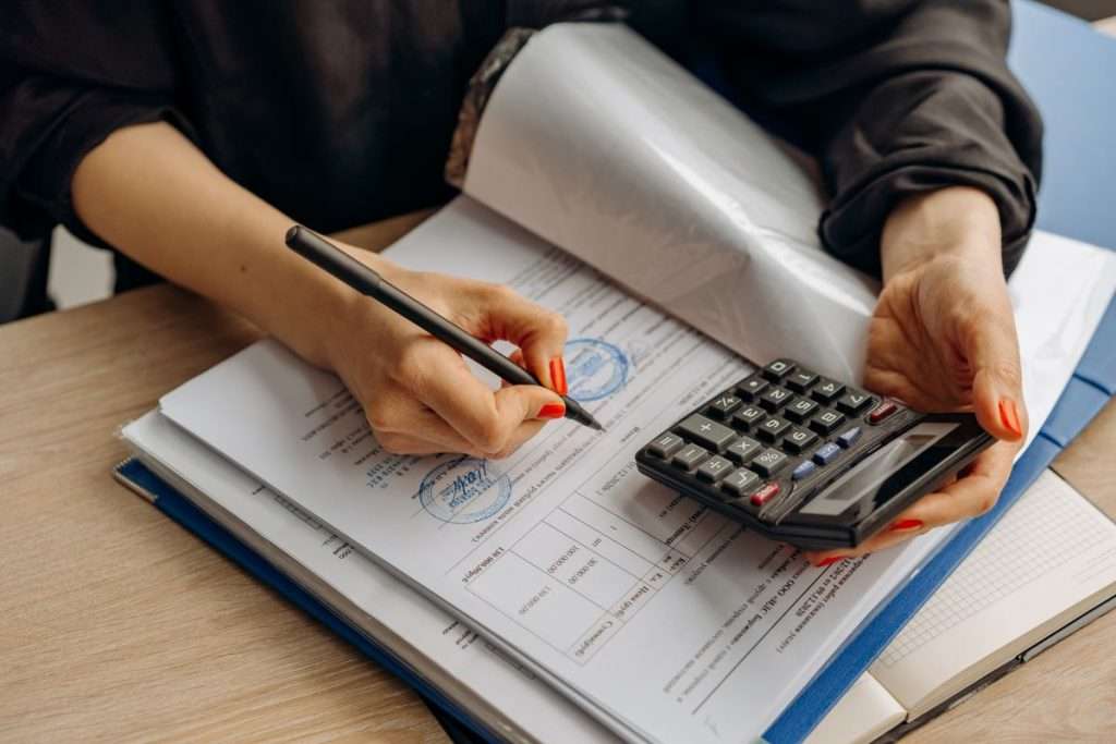 Contabilista a calcular valores e a assinar documentos numa secretária