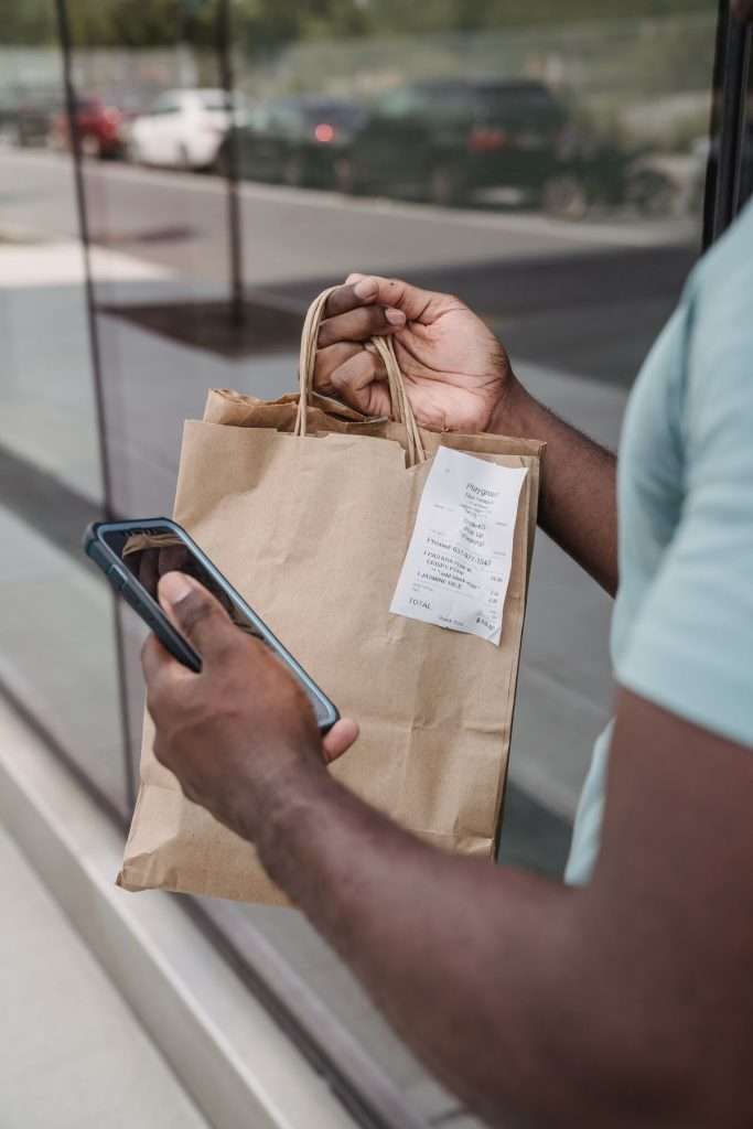 Pessoa a consultar um recibo digital no telemóvel junto de um saco de compras
