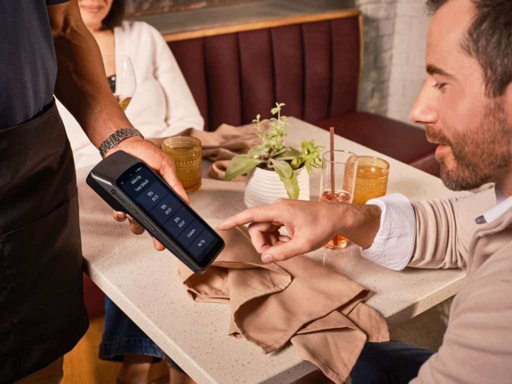 Empregado a apresentar um terminal de pagamento portátil numa mesa de restaurante
